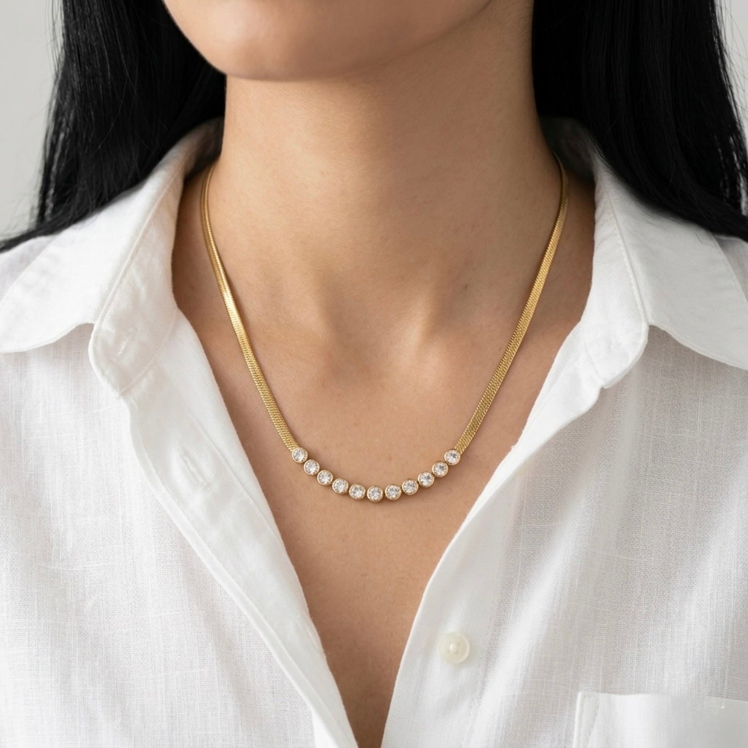 A gold-plated stainless steel snake chain necklace for women featuring a curved row of bezel-set crystals, shown on a model