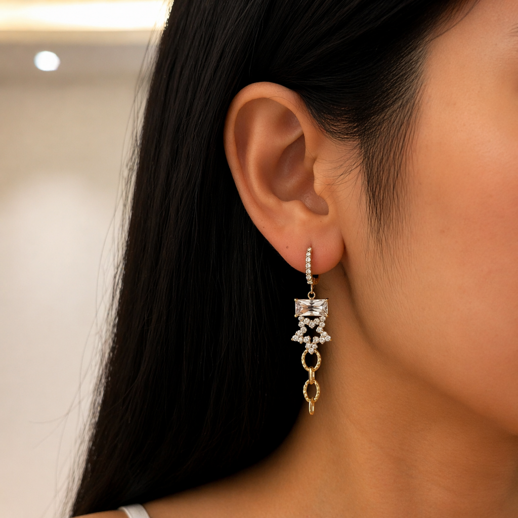 A gold-plated long earrings for women featuring an emerald-cut crystal, a star, and textured chain links, shown on a model