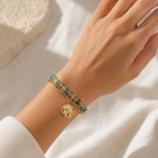 A gold-plated dual-layer ladies bracelet featuring a paperclip chain, green stones, and a textured starfish charm, shown on a model