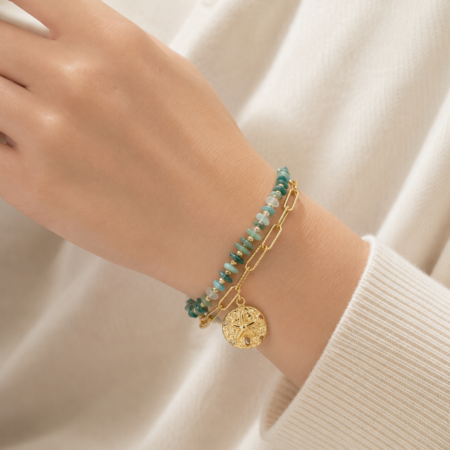 A gold-plated dual-layer ladies bracelet featuring a paperclip chain, green stones, and a textured starfish charm, shown on a model
