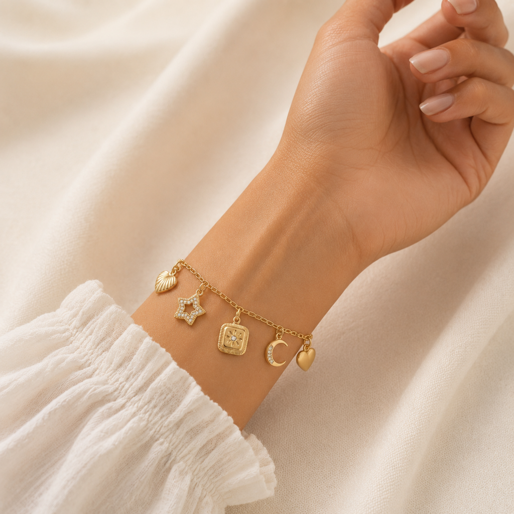 A gold-plated charm bracelet for women featuring five dangling celestial charms including a sun, star, moon, heart, and wing, shown on a model