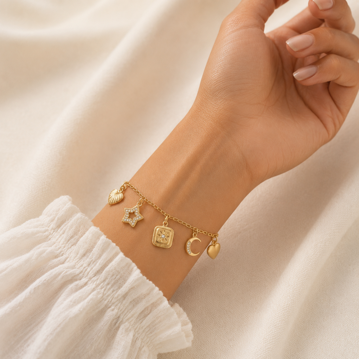 A gold-plated charm bracelet for women featuring five dangling celestial charms including a sun, star, moon, heart, and wing, shown on a model
