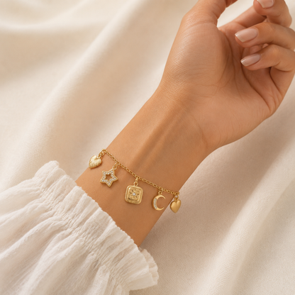A gold-plated charm bracelet for women featuring five dangling celestial charms including a sun, star, moon, heart, and wing, shown on a model