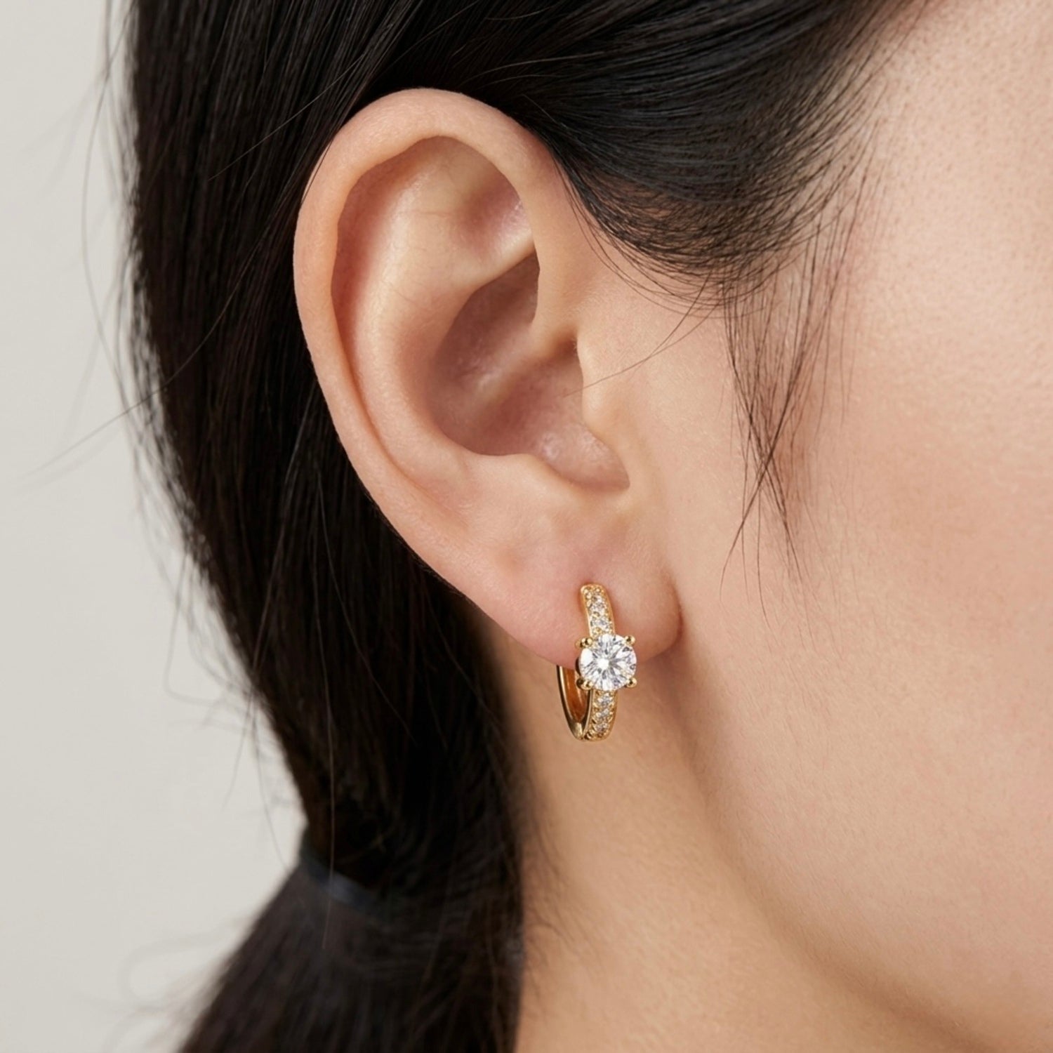 A gold-plated huggie hoop earrings for women featuring a prominent brilliant-cut central stone and pave crystal accents, shown on a model