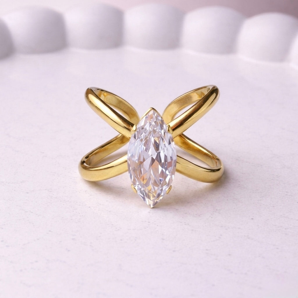 Gold plated adjustable statement ring for women featuring a large white-cut white stone crystal centered on a unique intersecting X-shaped band, displayed on a white background.