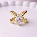 Gold plated adjustable statement ring for women featuring a large white-cut white stone crystal centered on a unique intersecting X-shaped band, displayed on a white background.