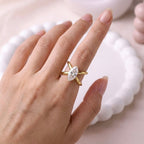 Gold plated adjustable statement ring for women featuring a large white-cut white stone crystal centered on a unique intersecting X-shaped band, displayed on a model hand