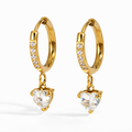 A pair of gold-plated hoop earrings for women featuring a sparkling heart-cut crystal drop, shown on a white background