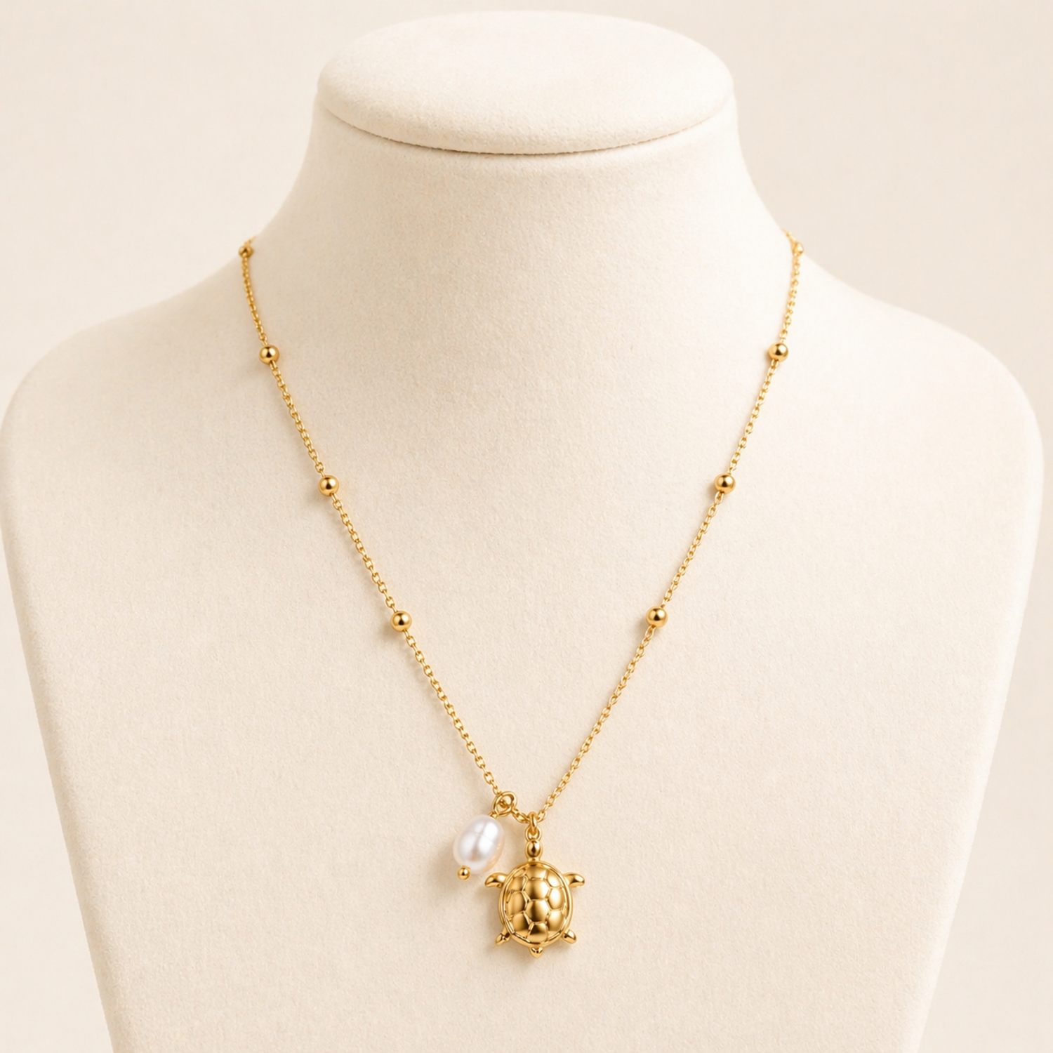 A close-view of a gold-plated stainless steel chain for women featuring small bead stations and a sea turtle pendant with a single pearl.