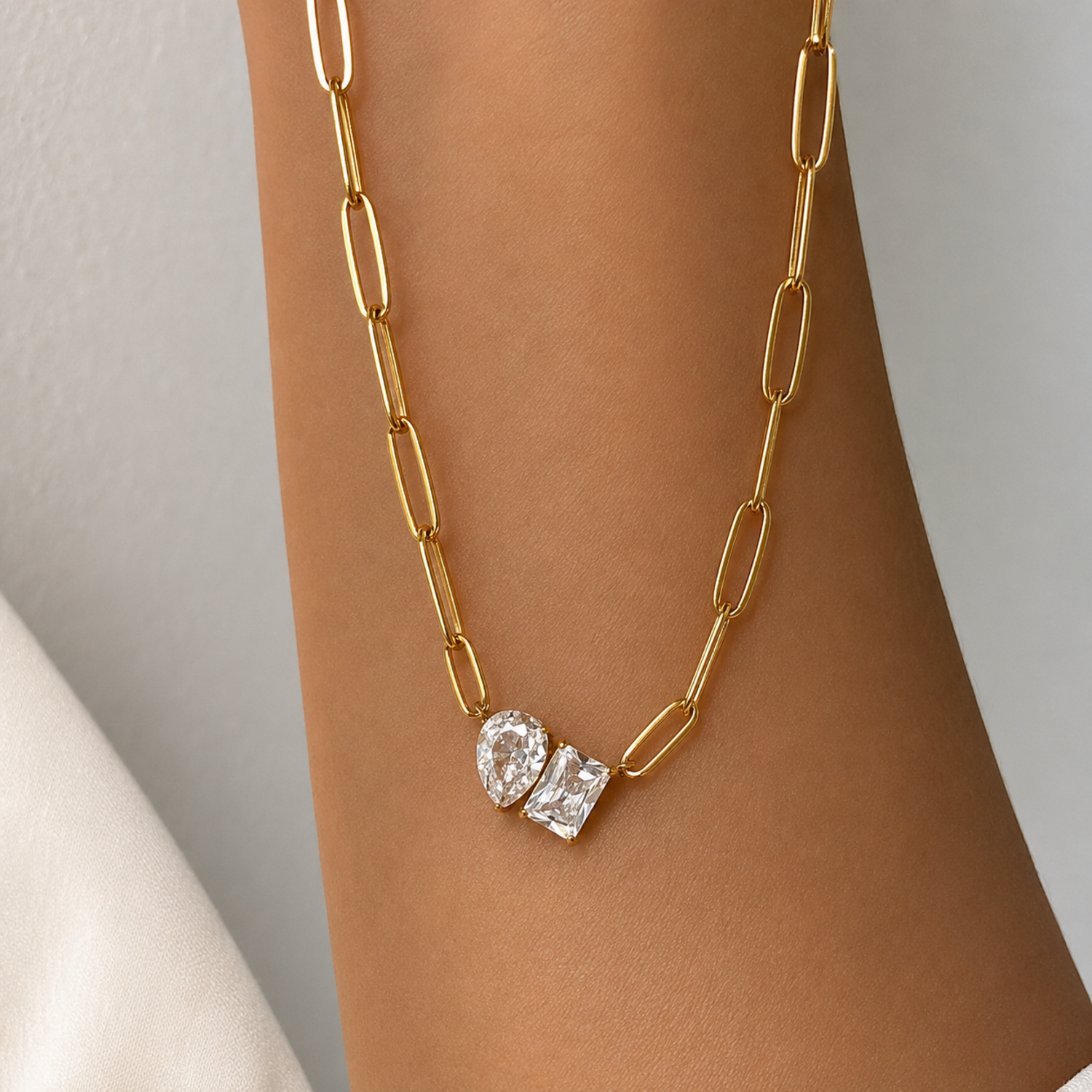 Gold chain necklace with diamond pendants on a person's wrist against a neutral background