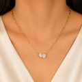 A gold-plated stainless steel chain for women featuring an elongated paperclip link design with a central pendant made of a pear-shape and emerald-shape stone joined together on a model