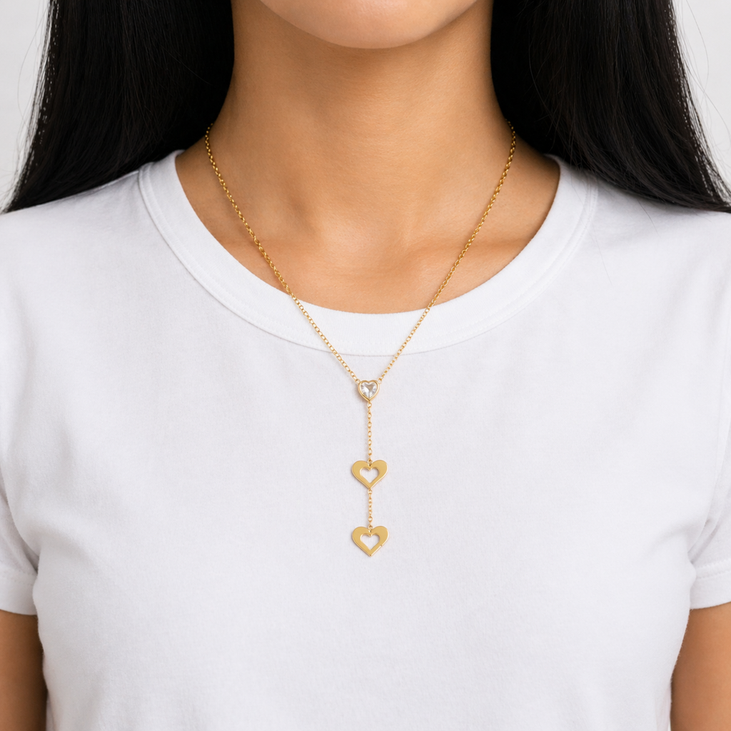 A gold-plated stainless steel chain for women featuring a heart-cut crystal and two open-heart charms in a cascading lariat style shown on a model