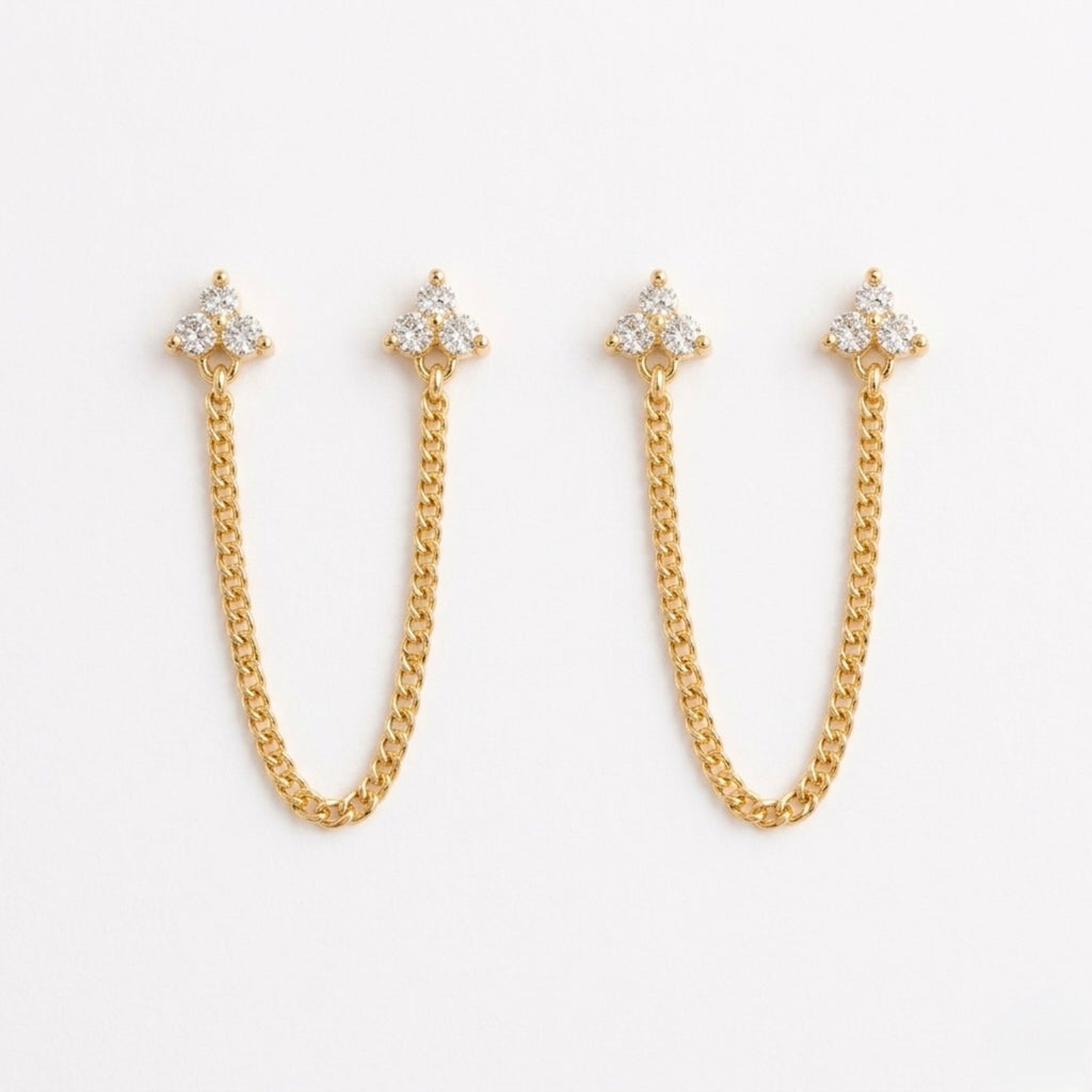 A pair of gold-plated ear chain earrings for women featuring two triple-stone white stone  blossom studs connected by a shimmering gold chain on a white background