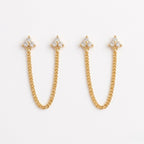 A pair of gold-plated ear chain earrings for women featuring two triple-stone white stone  blossom studs connected by a shimmering gold chain on a white background