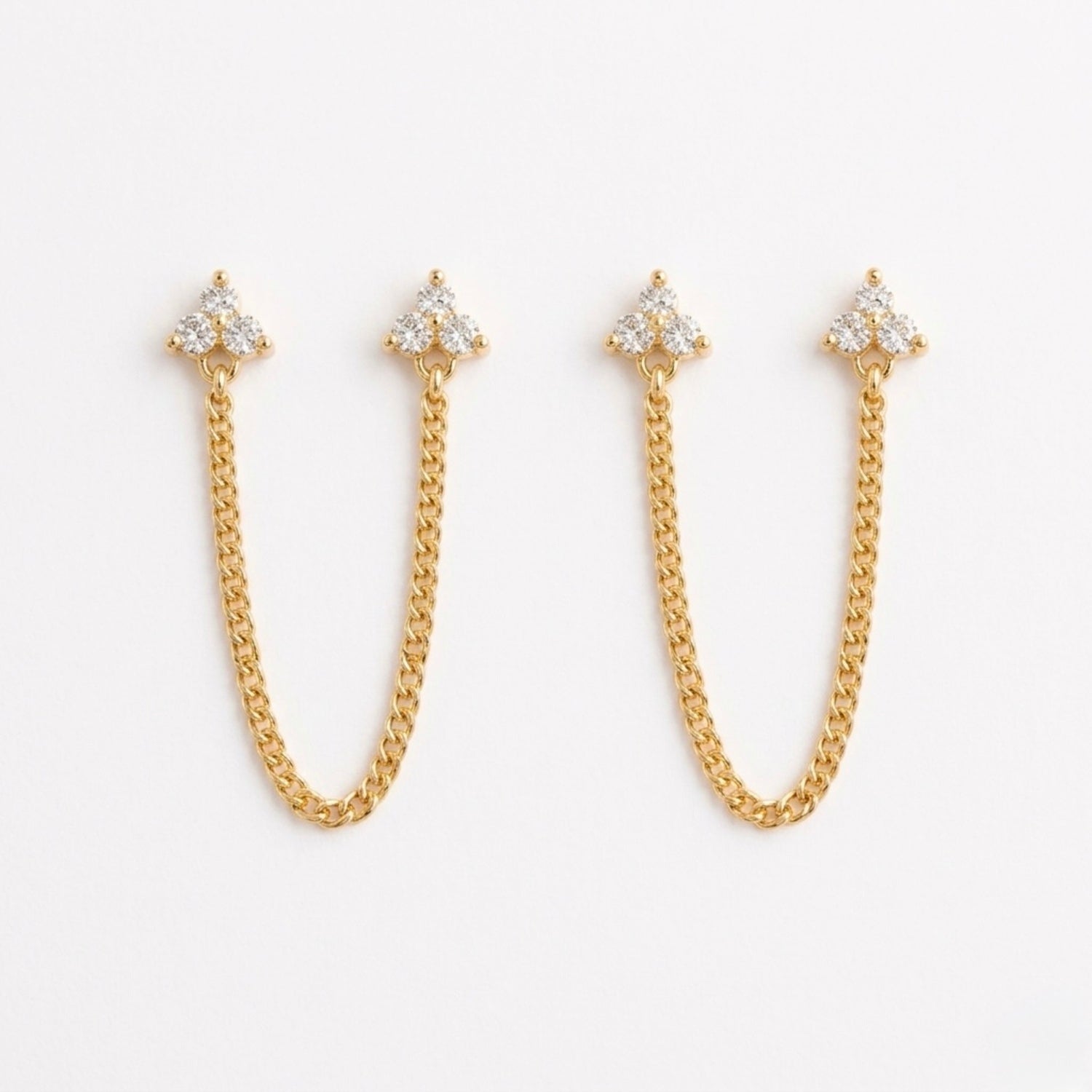 A pair of gold-plated ear chain earrings for women featuring two triple-stone white stone  blossom studs connected by a shimmering gold chain on a white background