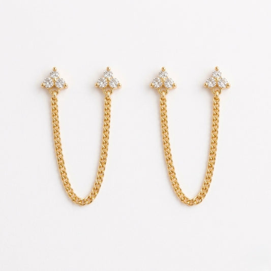 A pair of gold-plated ear chain earrings for women featuring two triple-stone white stone  blossom studs connected by a shimmering gold chain on a white background