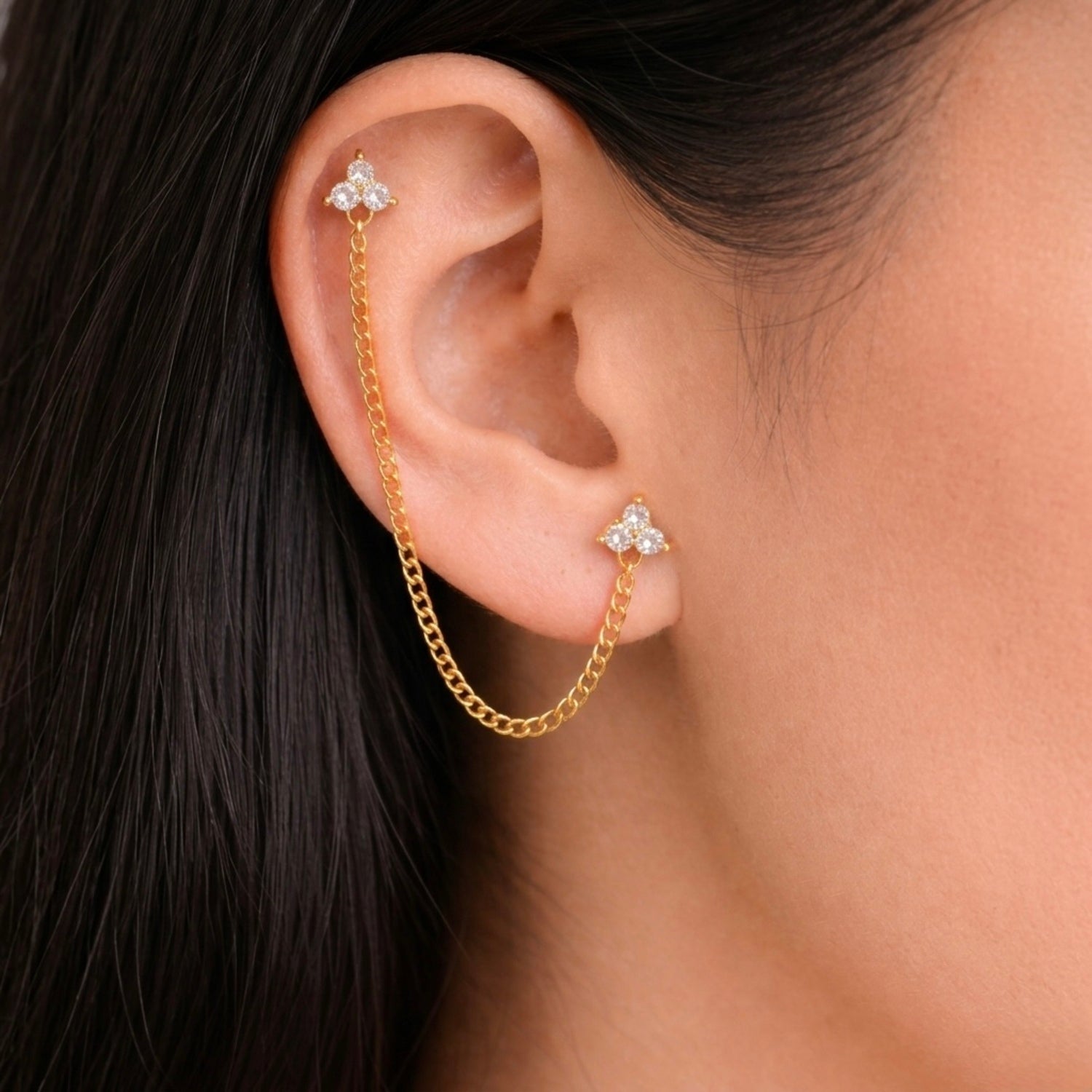 A gold-plated ear chain earrings for women featuring two triple-stone white stone  blossom studs connected by a shimmering gold chain on a model