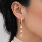 A gold-plated long earrings for women featuring a rectangular hoop and three dangling pear-cut crystals, shown on a model