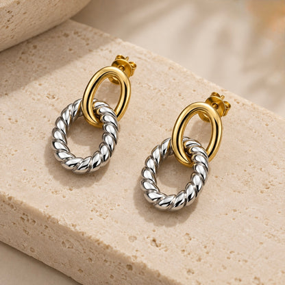 Two-tone earrings for women featuring a gold plated oval hoop and silver twisted loop design on a beige textured surface