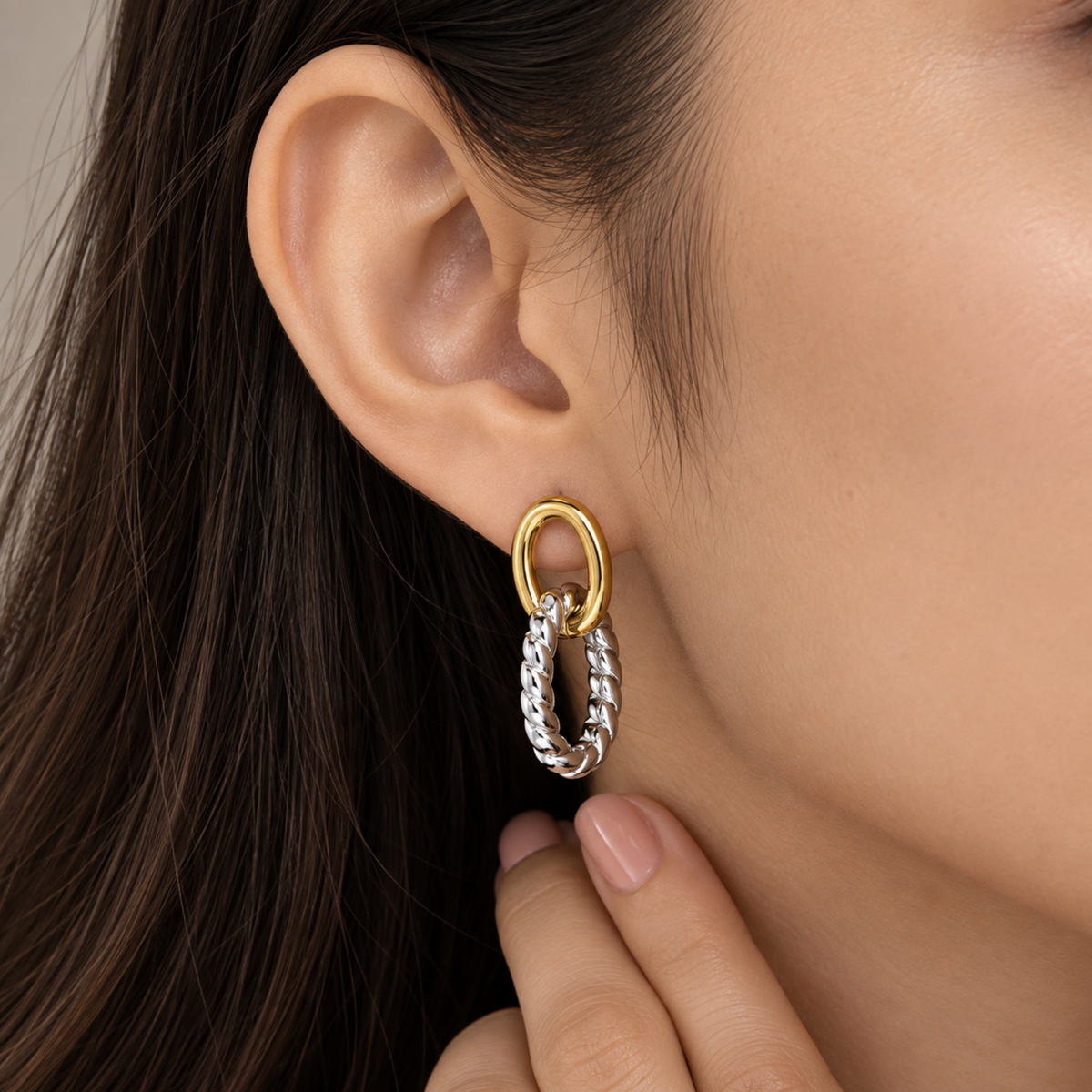 A close-up of a model's ear wearing a gold hoop earring with a dangling textured silver hoop.
