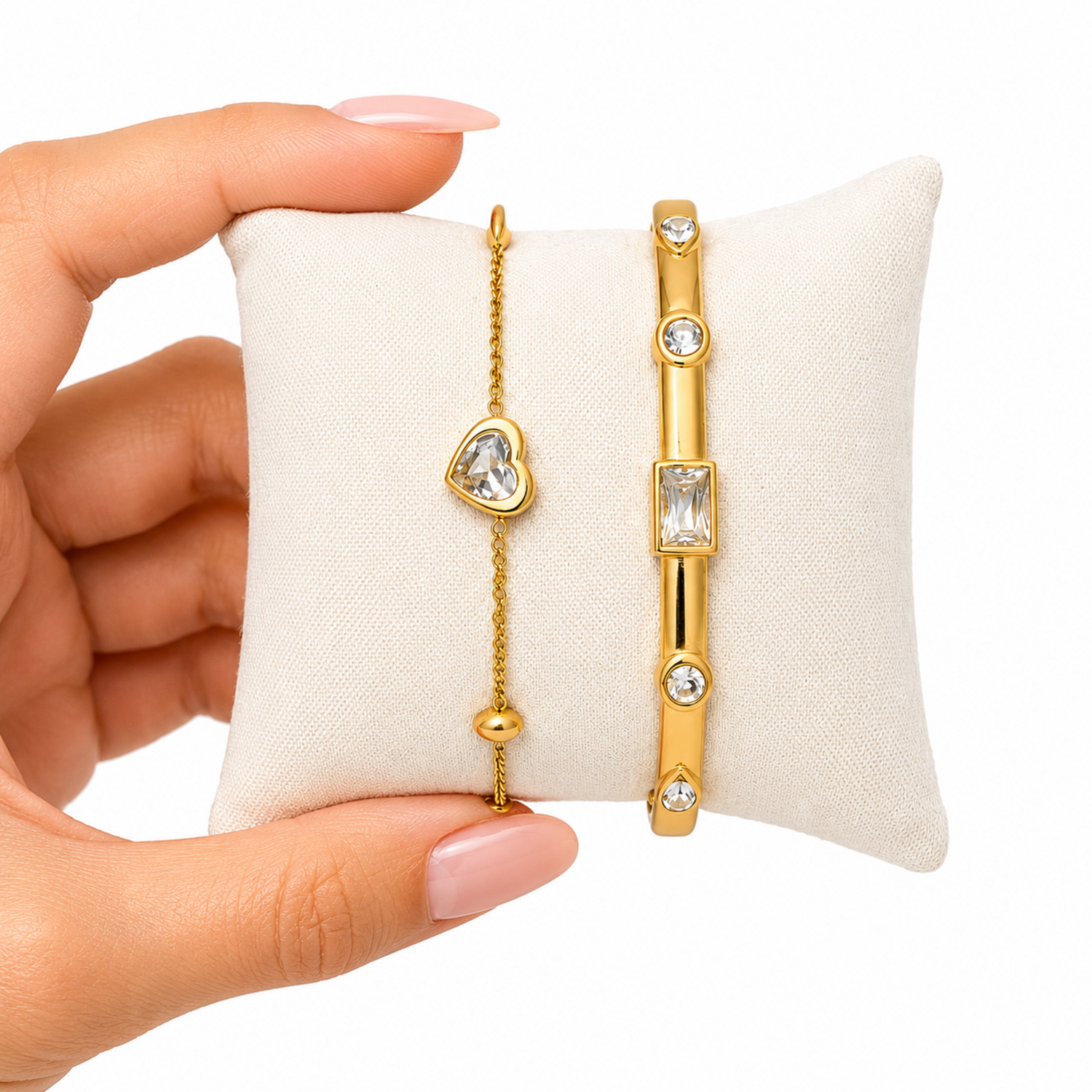 A close-view of a premium two-piece gold-plated bracelet stack for women featuring a gold baguette station bangle and a fine link chain with a single heart crystal charm