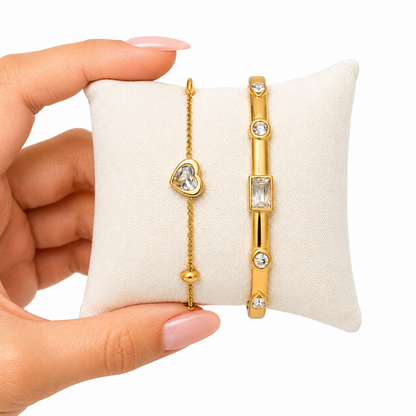 A close-view of a premium two-piece gold-plated bracelet stack for women featuring a gold baguette station bangle and a fine link chain with a single heart crystal charm