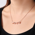 Rose gold necklace with heart pendants on a person wearing a black top.