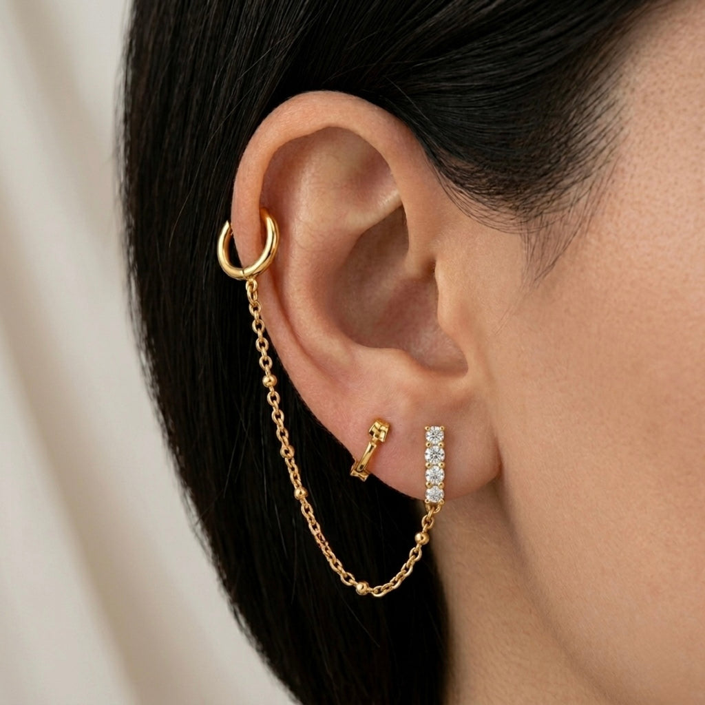 A gold-plated ear chain earrings for women connecting a shimmering crystal bar stud to a small gold hoop with a fine chain on a model