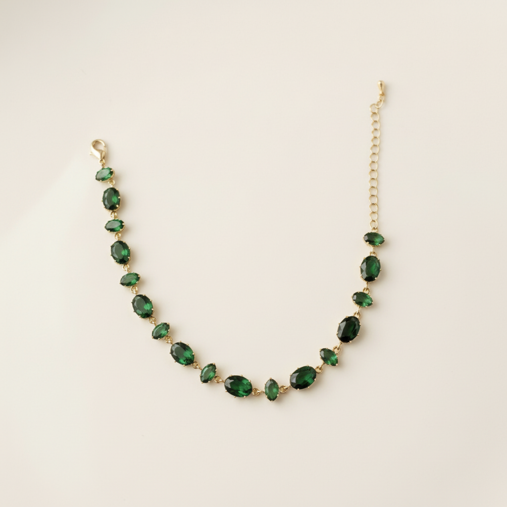 A gold-plated chain bracelet for women featuring a continuous row of deep emerald green oval-cut stones on a clean cream background