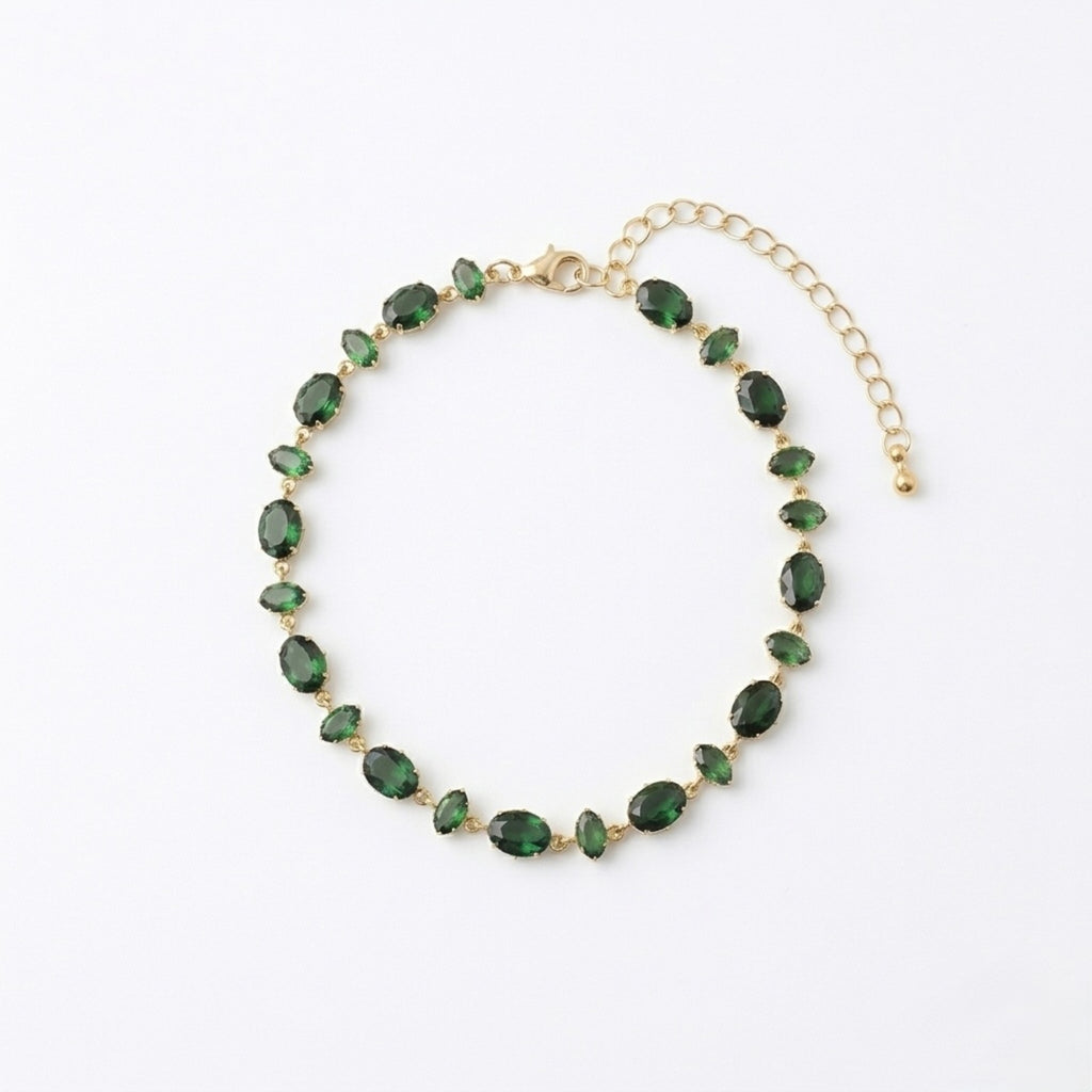 A gold-plated chain bracelet for women featuring a continuous row of deep emerald green oval-cut stones on a clean white background