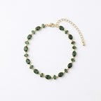 A gold-plated chain bracelet for women featuring a continuous row of deep emerald green oval-cut stones on a clean white background