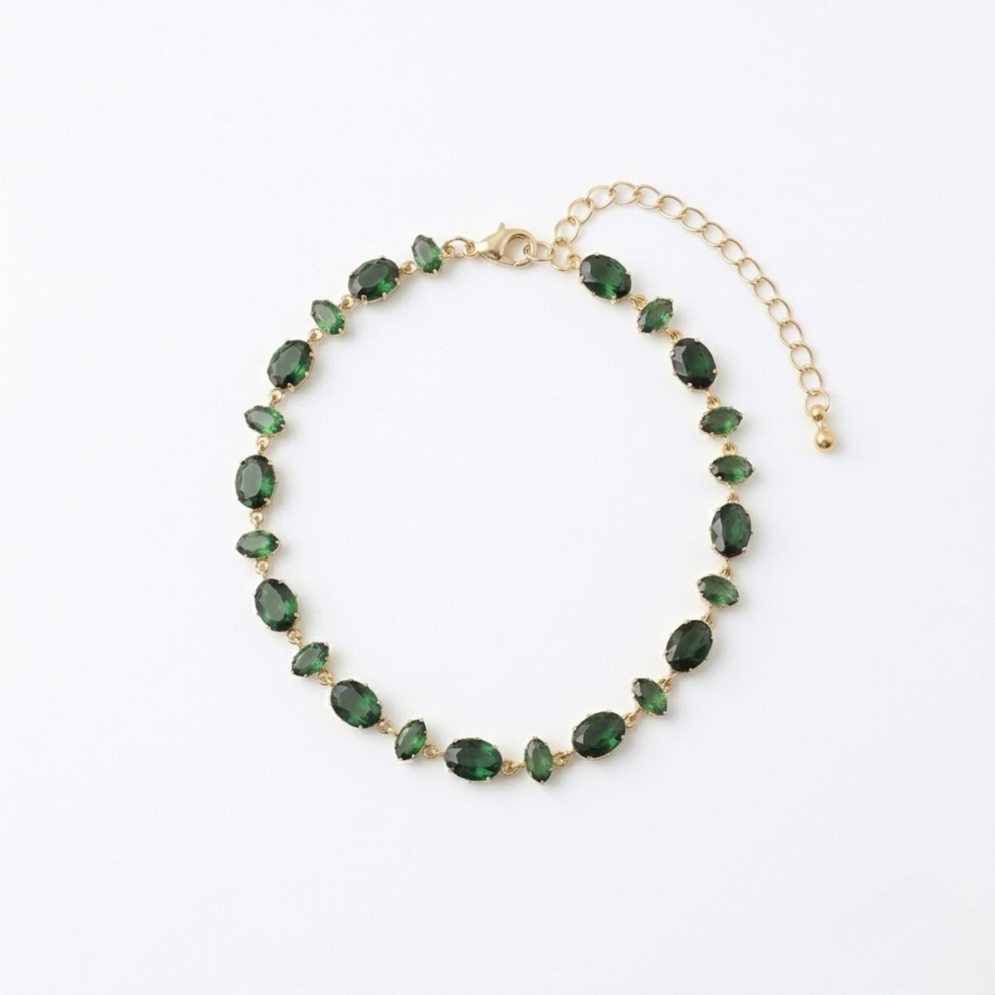 A gold-plated chain bracelet for women featuring a continuous row of deep emerald green oval-cut stones on a clean white background