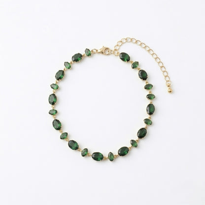 A gold-plated chain bracelet for women featuring a continuous row of deep emerald green oval-cut stones on a clean white background