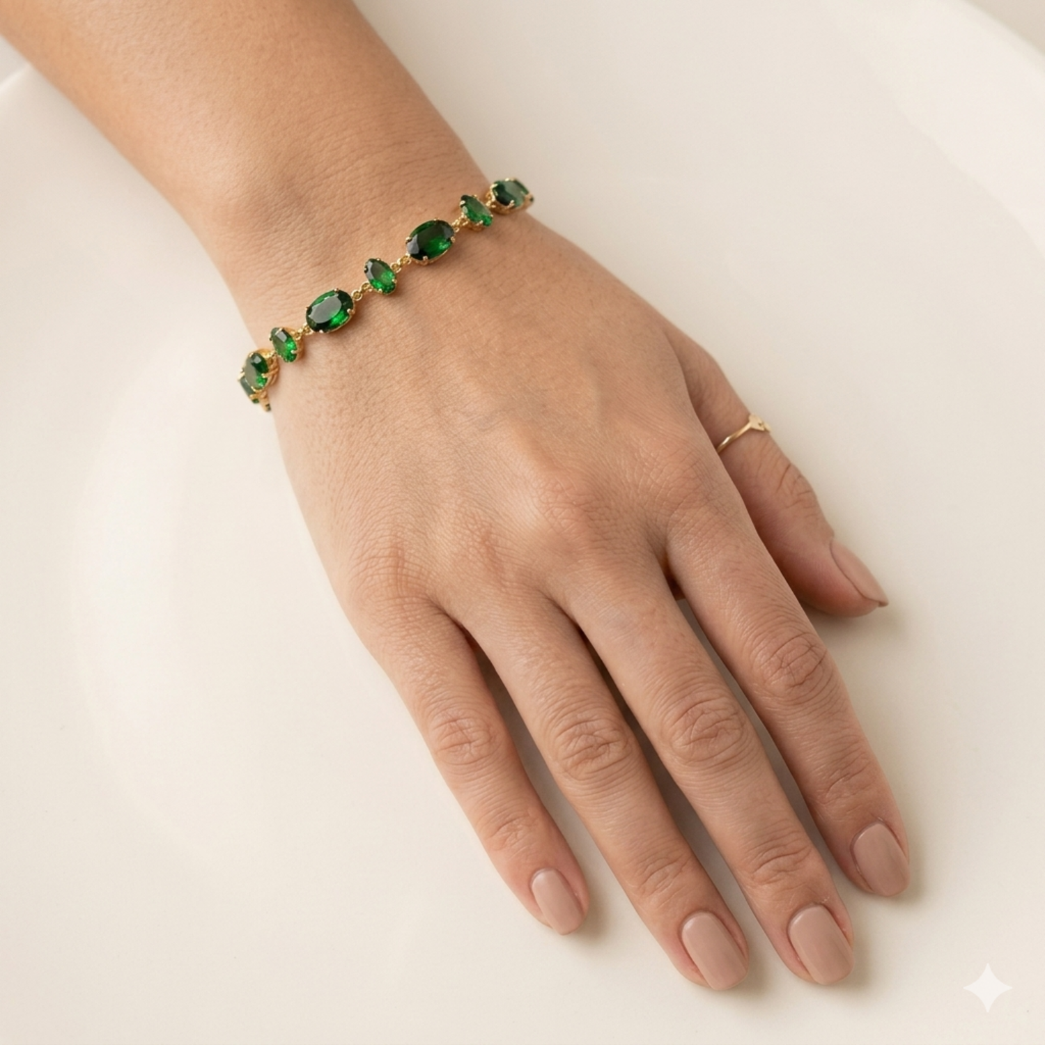 A gold-plated chain bracelet for women featuring a continuous row of deep emerald green oval-cut stones on a model hand