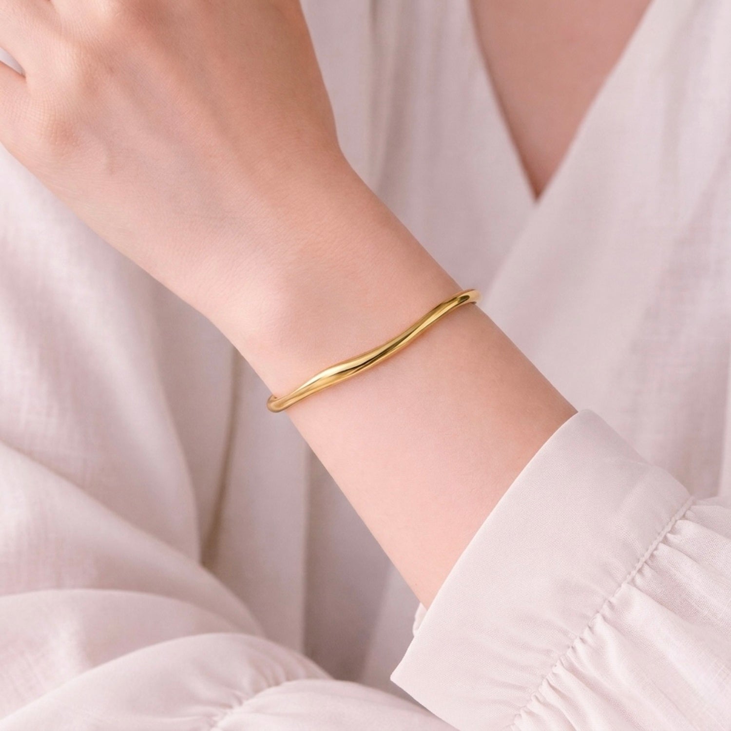 A minimalist gold-plated twisted cuff bracelet for women featuring wave design displayed on a model hand