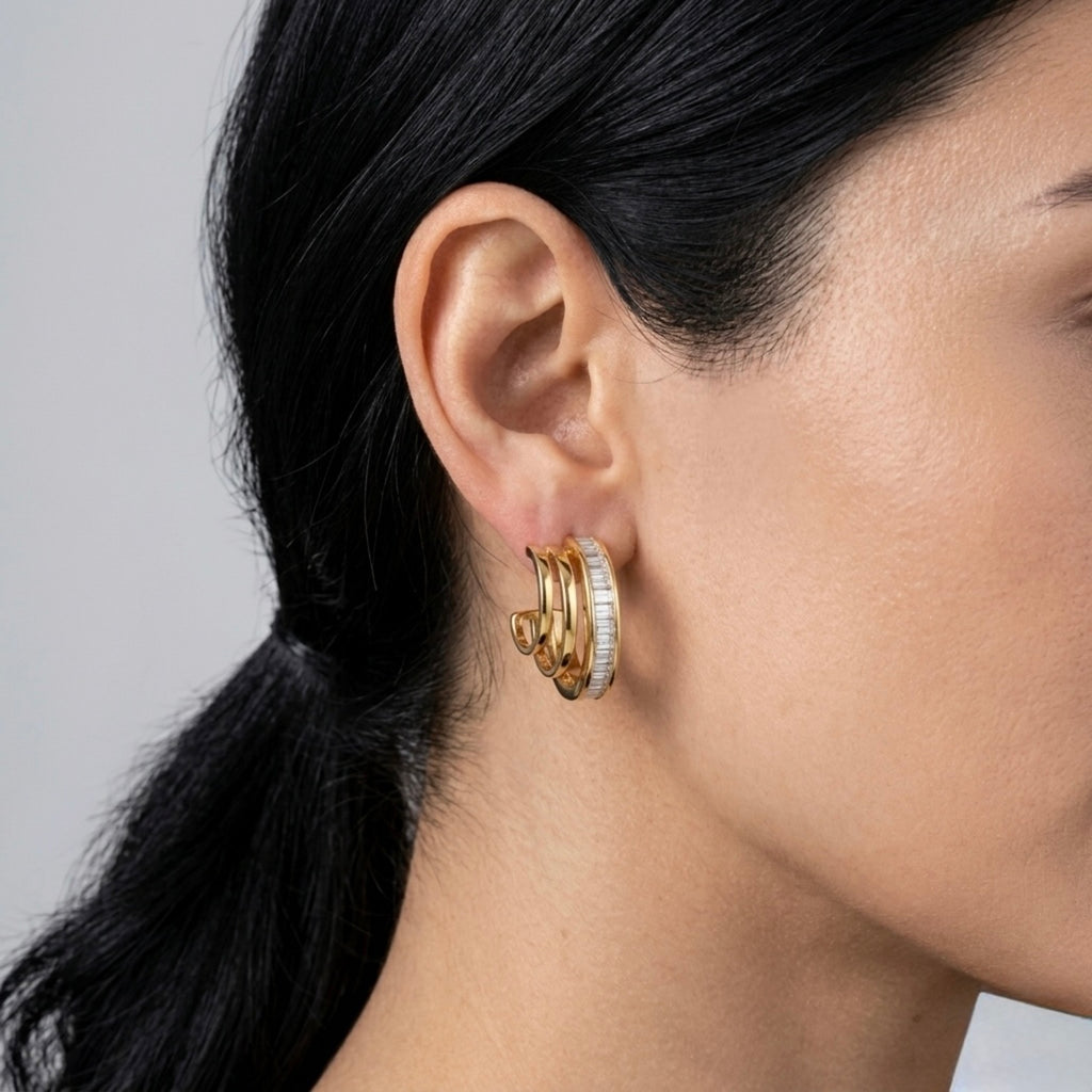 A gold-plated triple-band hoop earrings for women featuring a central row of clear baguette crystals, shown on a model