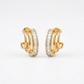 A pair of gold-plated triple-band hoop earrings for women featuring a central row of clear baguette crystals, shown on a clean white background.