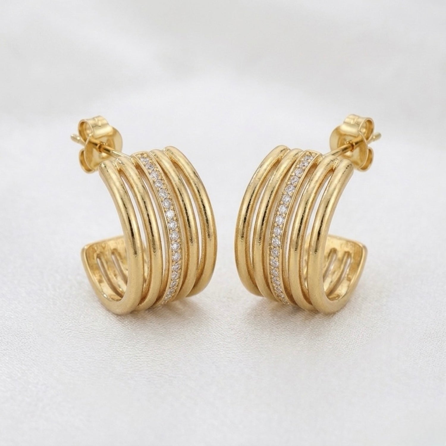 A pair of gold-plated multi-band hoop earrings for women featuring a central row of clear pavé crystals, shown on a white background.