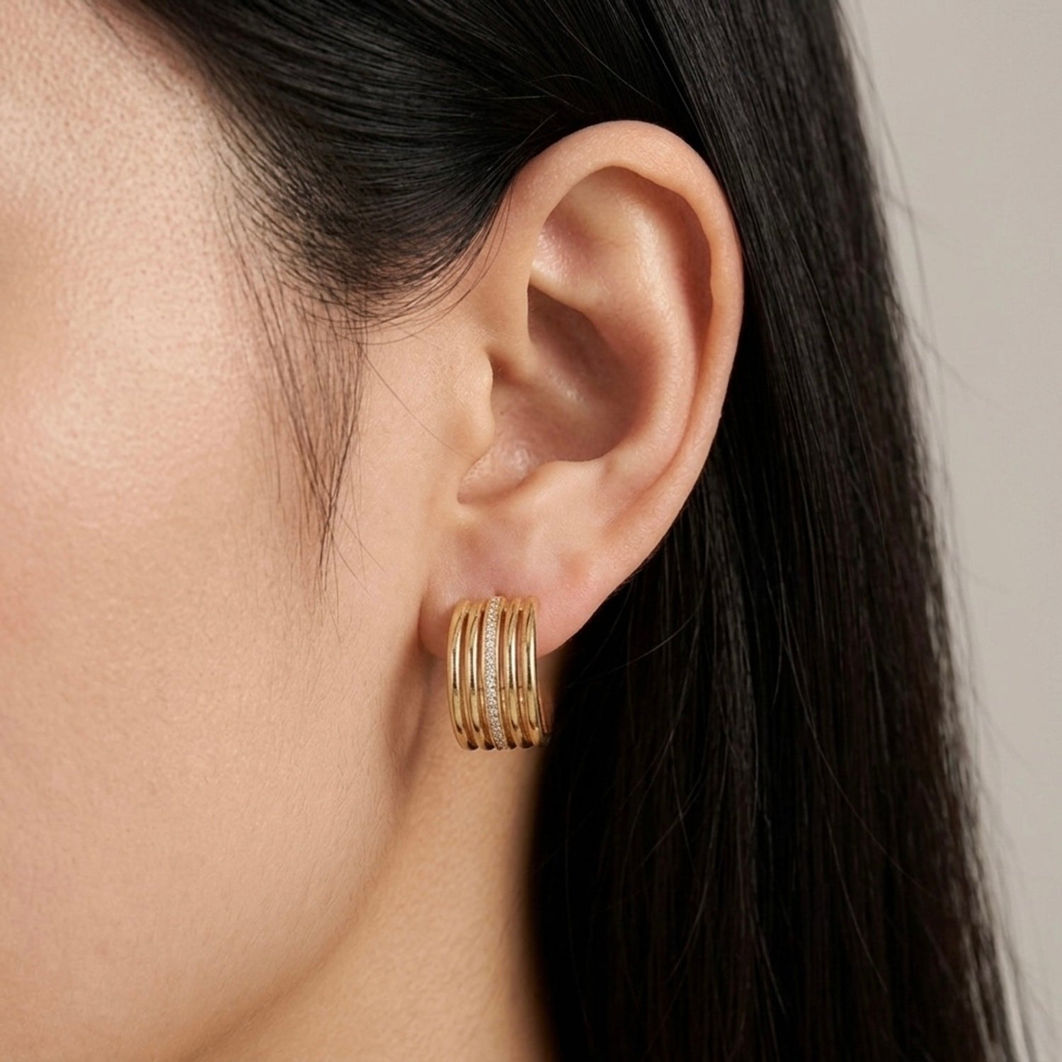 A gold-plated multi-band hoop earrings for women featuring a central row of clear pavé crystals, shown on a model