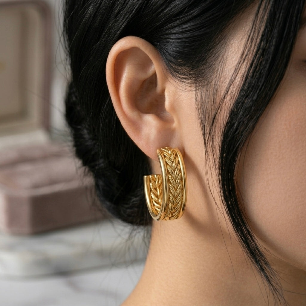 A gold-plated wide-band open hoop earrings for women featuring a detailed central braided wheat design, shown on a model