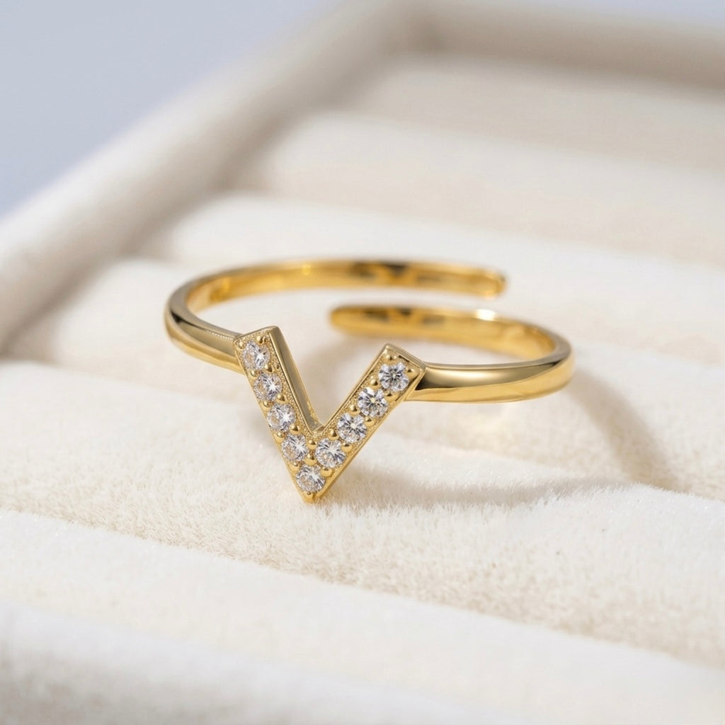 A modern gold plated adjustable ring for women featuring a "V" shaped chevron design encrusted with small shimmering on a jewellery box