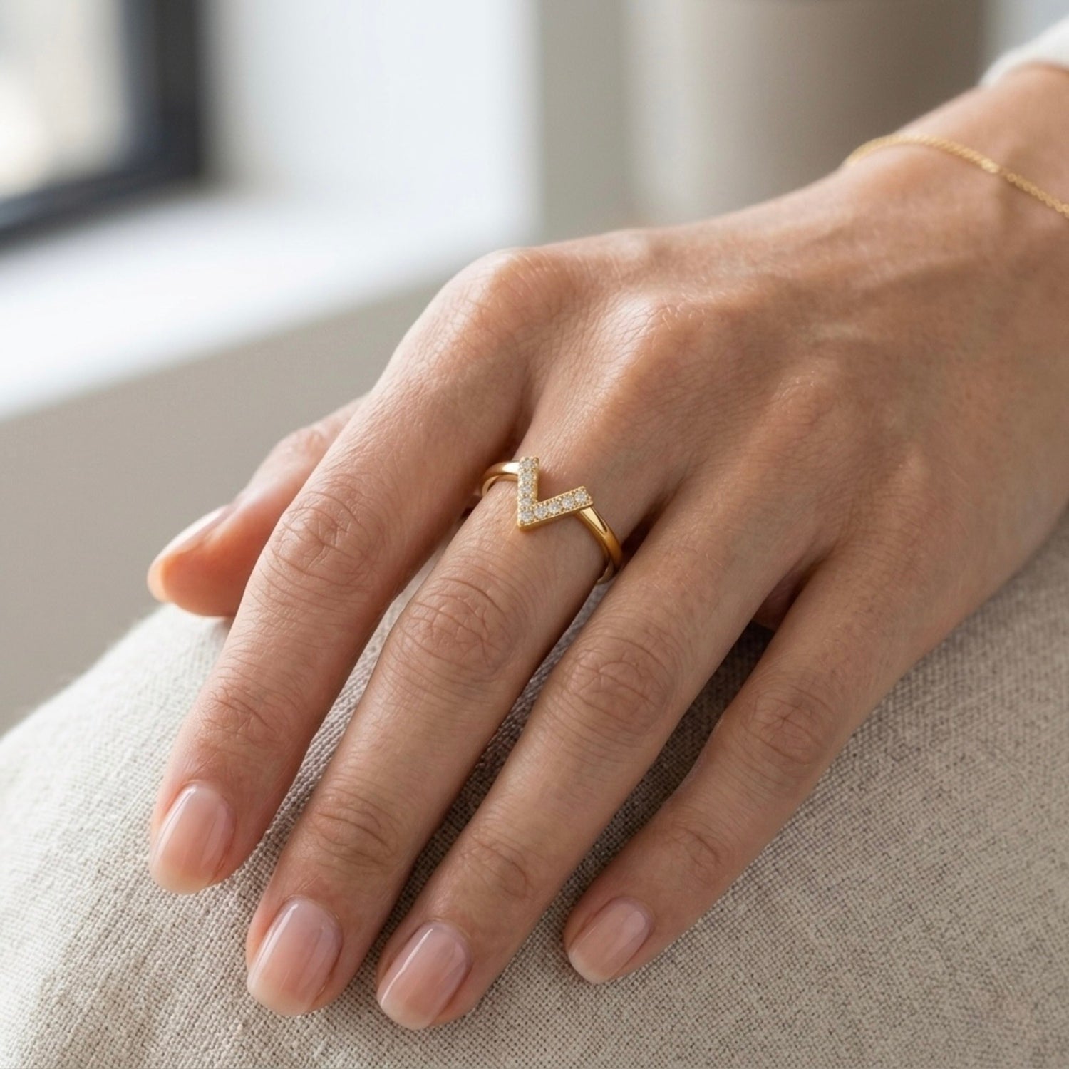 A modern gold plated adjustable ring for women featuring a "V" shaped chevron design encrusted with small shimmering crystals on a model hand