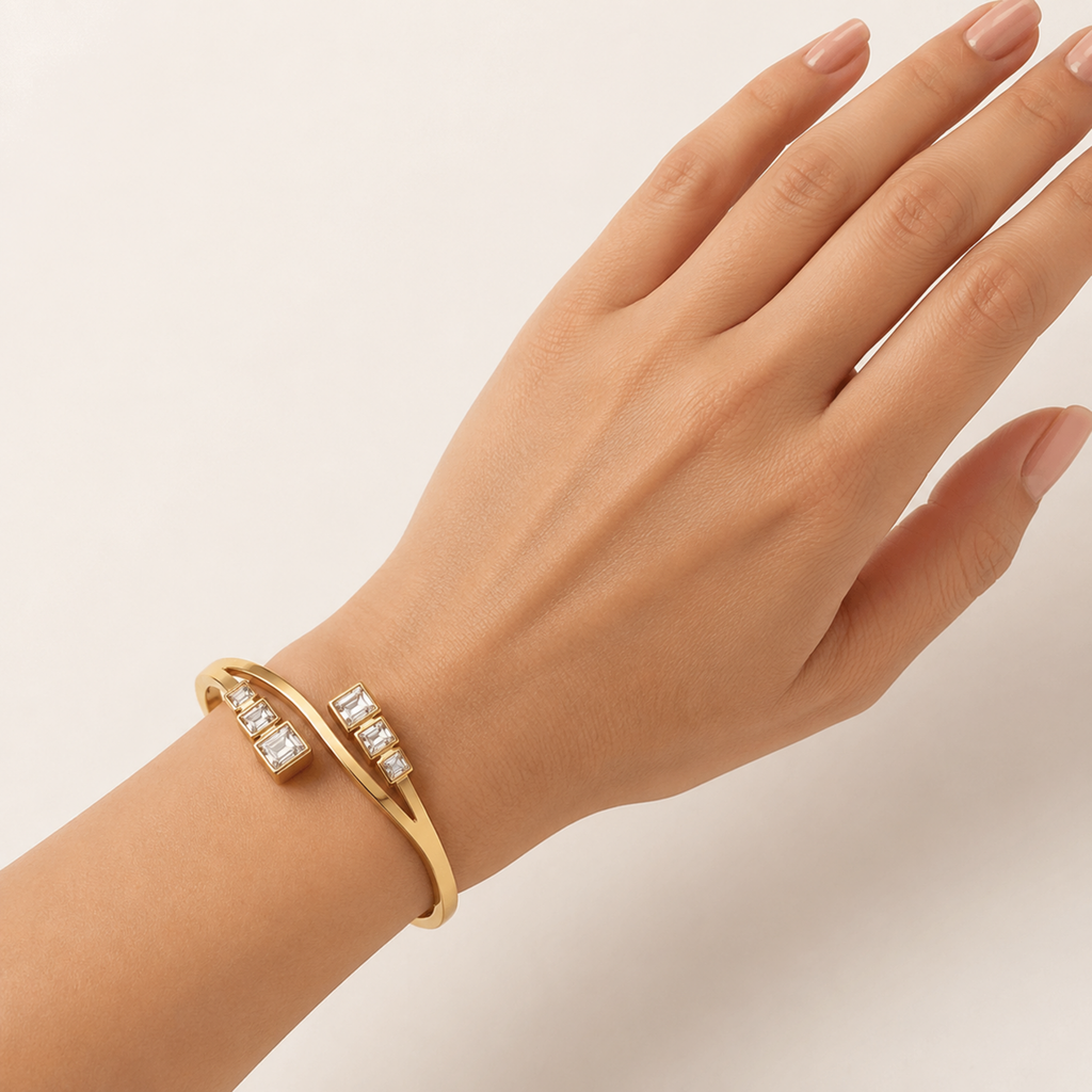 A close-view gold-plated crossover bypass bangle for women featuring graduated baguette-cut crystals and a secure side-clasp.