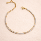 A close view of a  delicate, thin gold-plated tennis bracelet for women shown on a cream background