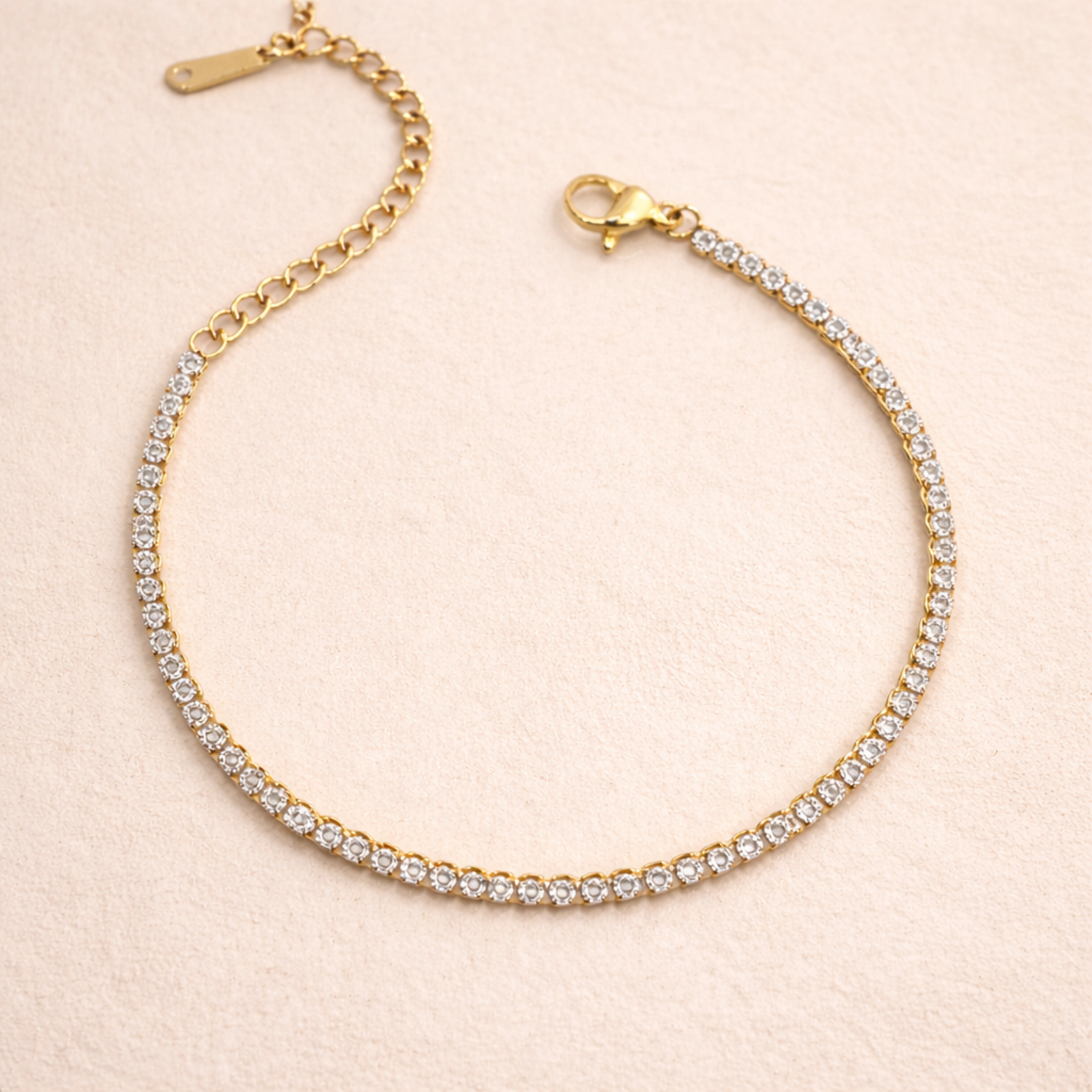 A close view of a  delicate, thin gold-plated tennis bracelet for women shown on a cream background
