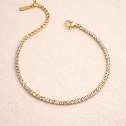 A close view of a  delicate, thin gold-plated tennis bracelet for women shown on a cream background