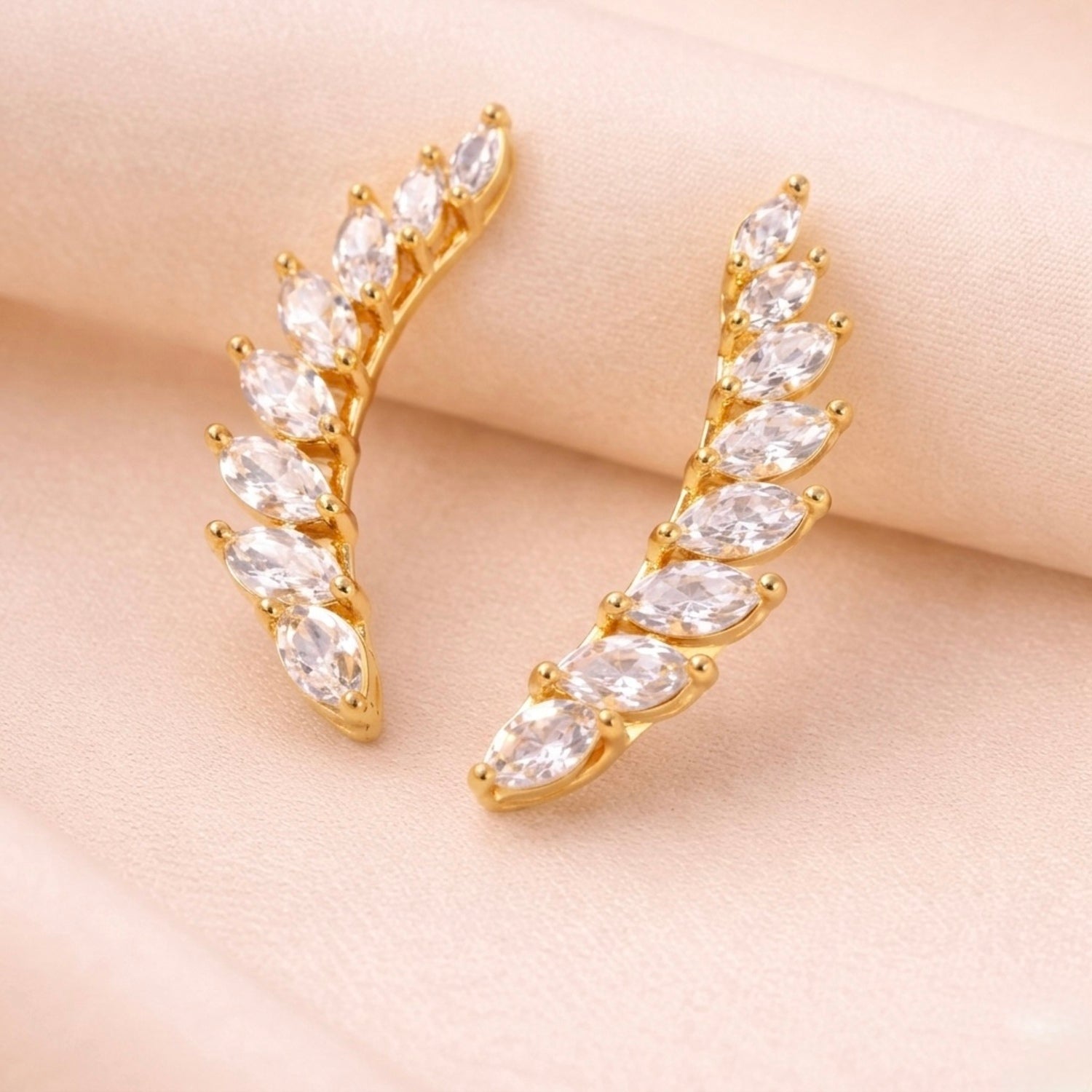 A pair of of gold-plated celestial Zenith Starburst ear climber earrings for women featuring stones and a star motif on a beige background